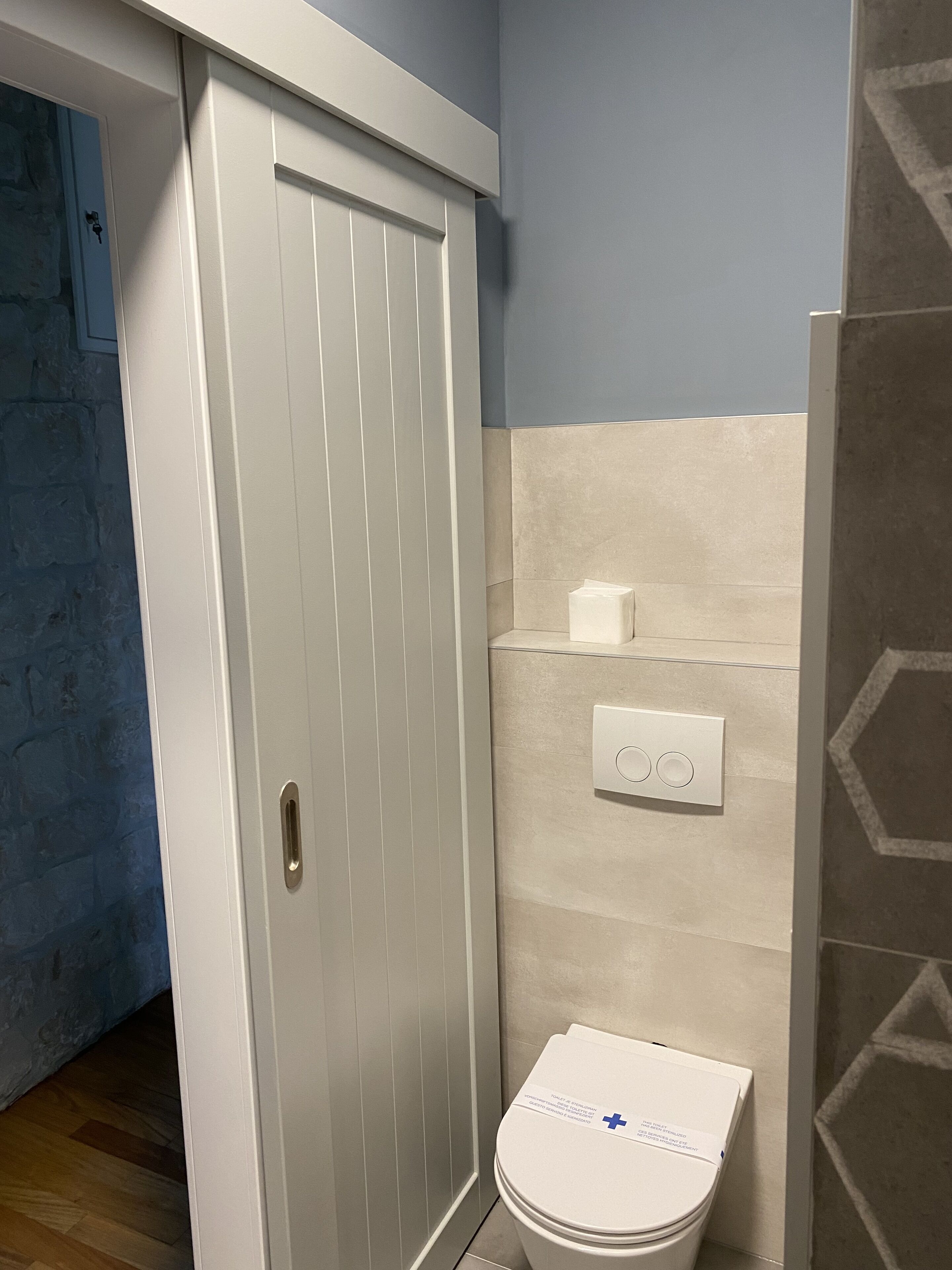 Un baño con una puerta blanca, un inodoro, un interruptor de luz en la pared y un dispensador de toallas.