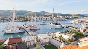 Un port de plaisance où sont amarrés de nombreux bateaux, entouré de bâtiments et avec des collines en arrière-plan.