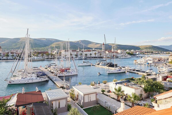 A marina with multiple boats docked, surrounded by buildings and hills in the background.