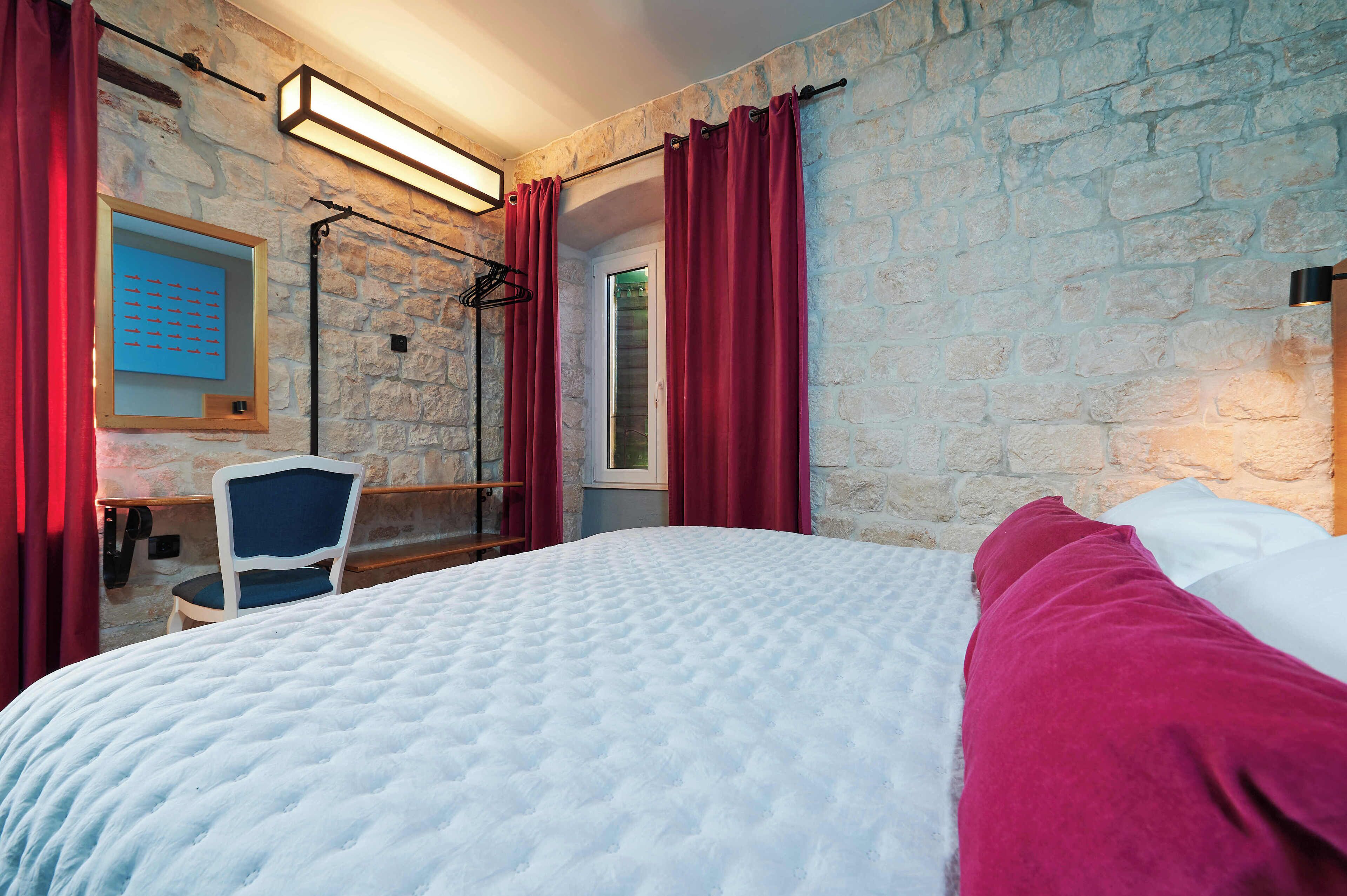 A bedroom with a bed, a chair, a desk, and a stone wall.