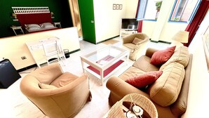 A living room with a sofa, armchair, and a coffee table. There is a TV on a stand and a door leading to another room. - Hotel Conde de Cárdenas (Córdoba)