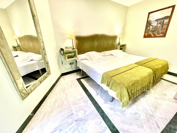 Una habitación de hotel con cama, mesitas de noche, un espejo y un cuadro en la pared.