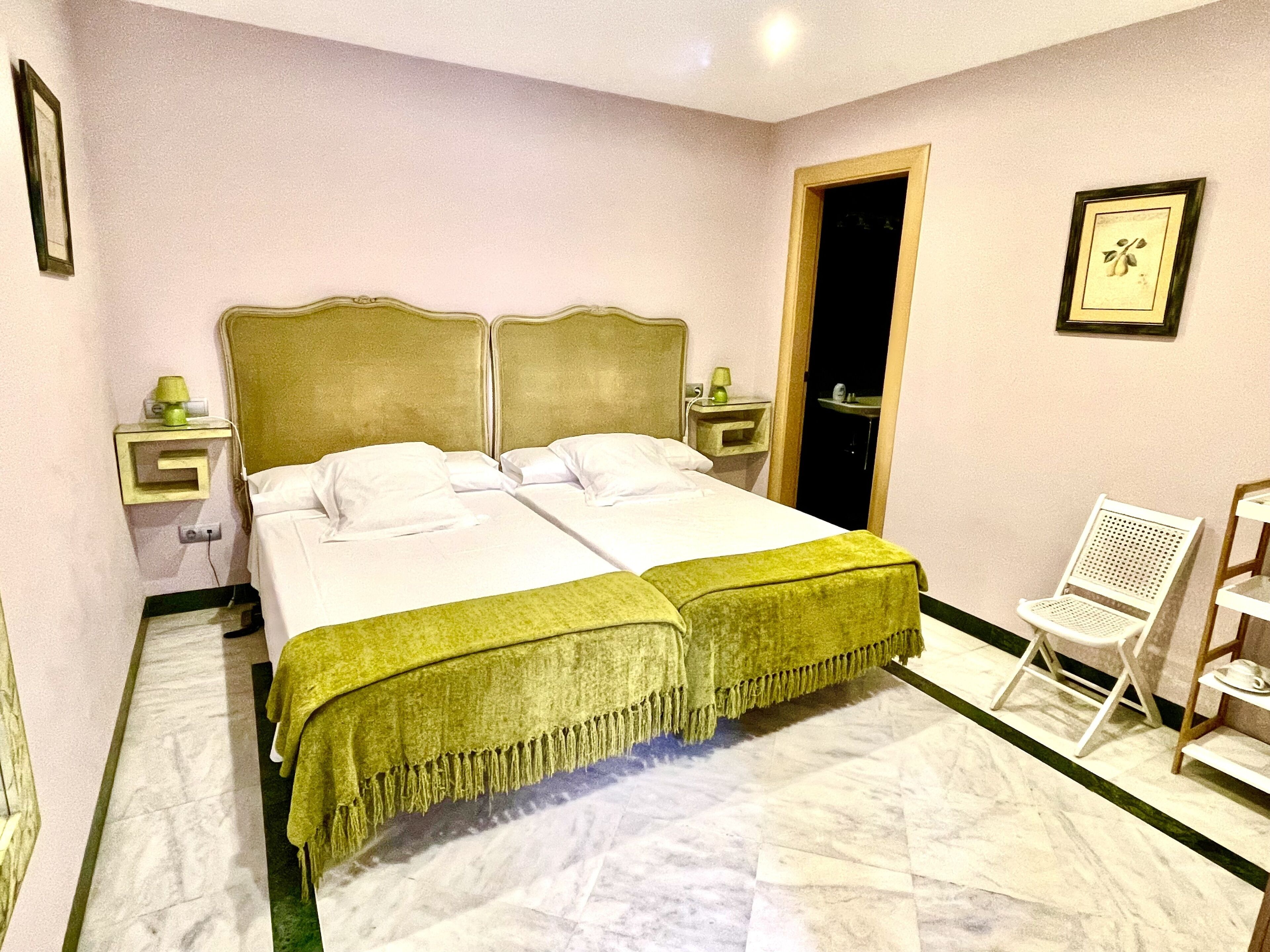 A double bed with a green bedspread, two bedside tables, a chair, and a door to a bathroom.