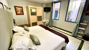 A bedroom with a large bed, a wardrobe, a desk, and a window with a view of greenery. - Hotel Conde de Cárdenas (Córdoba)