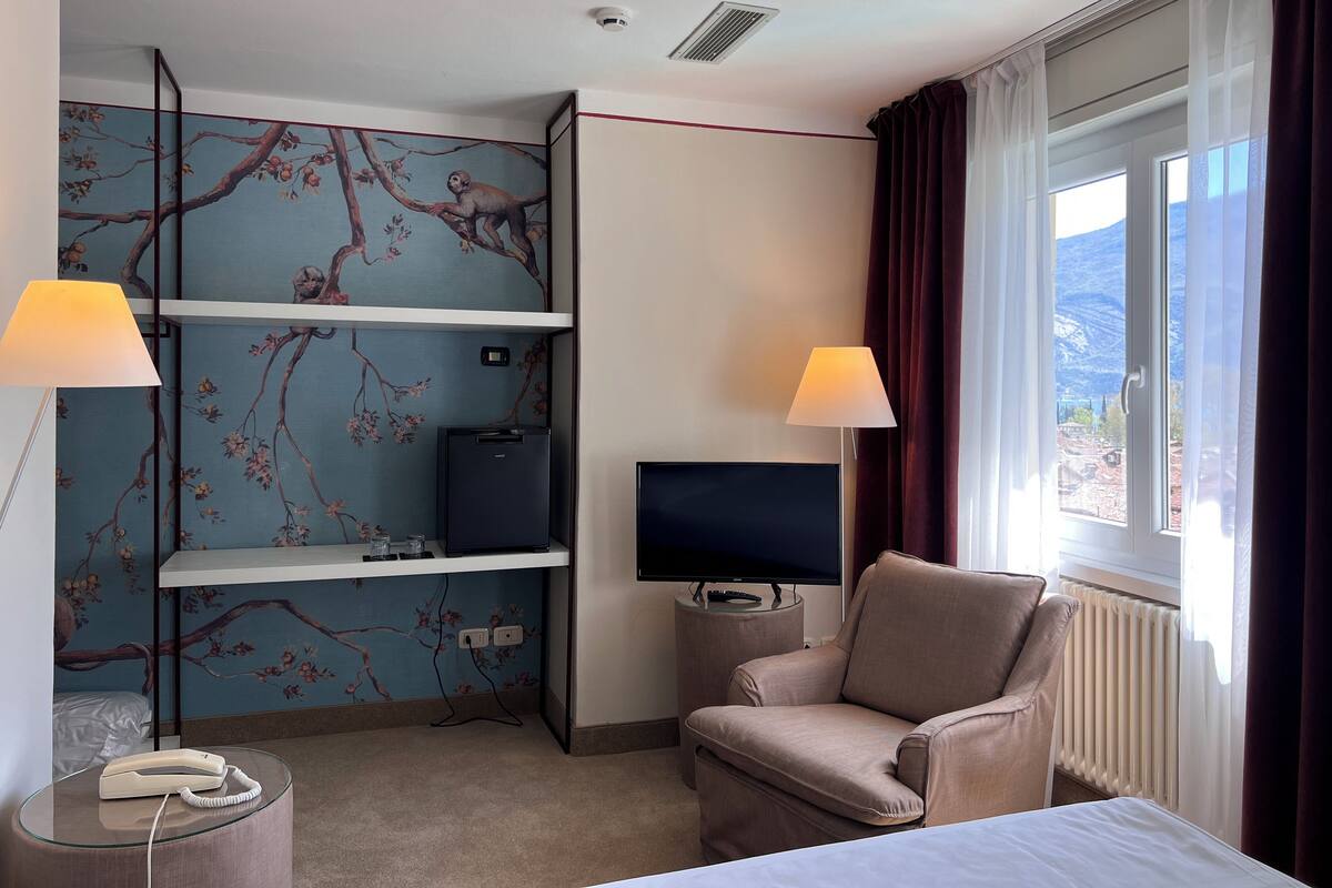 Habitación de hotel con cama, televisión, una silla, escritorio con lámpara y teléfono.