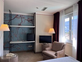 Habitación de hotel con cama, televisión, una silla, escritorio con lámpara y teléfono.