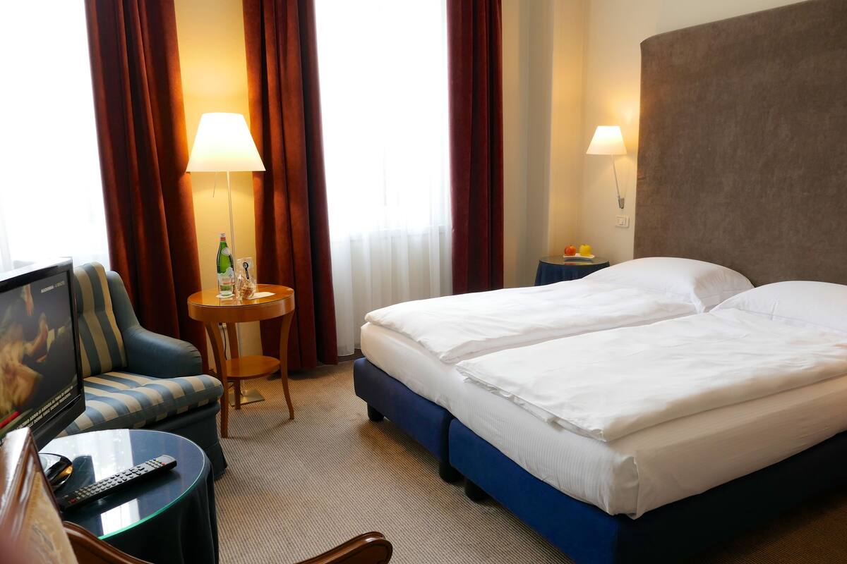 Una habitación de hotel con una cama, televisión, una silla, una mesita y una lámpara.
