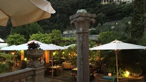 An outdoor patio area with stone columns, wicker furniture, and umbrellas providing shade.