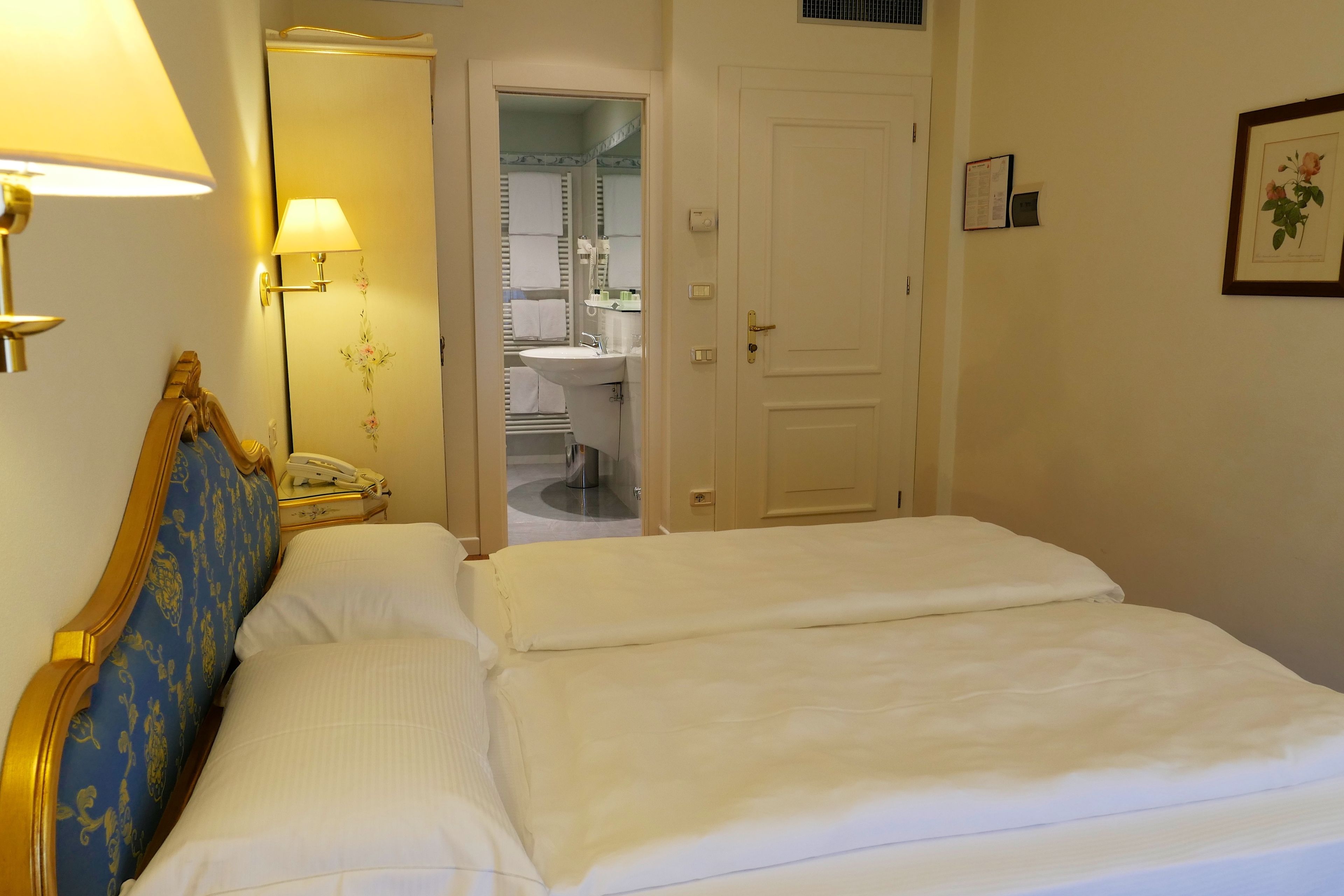 Ein Hotelzimmer mit Bett, Nachttischlampe, Telefon und einem durch eine offene Tür einsehbaren Badezimmer.