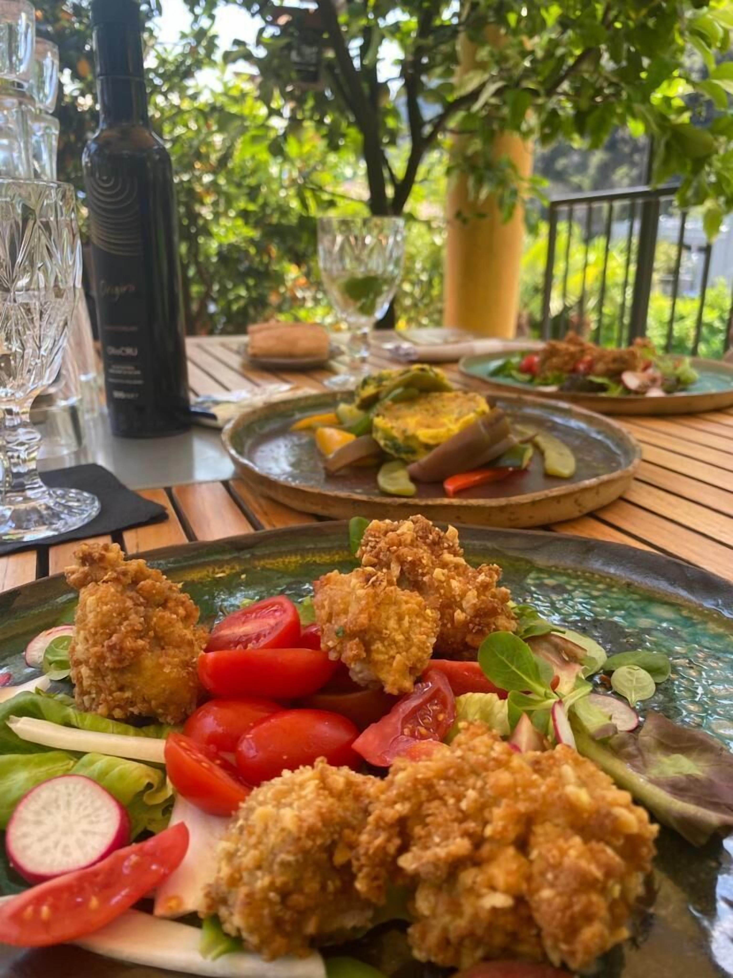 A table set with a salad, fried chicken, and a bottle of wine, with a view of greenery in the background.