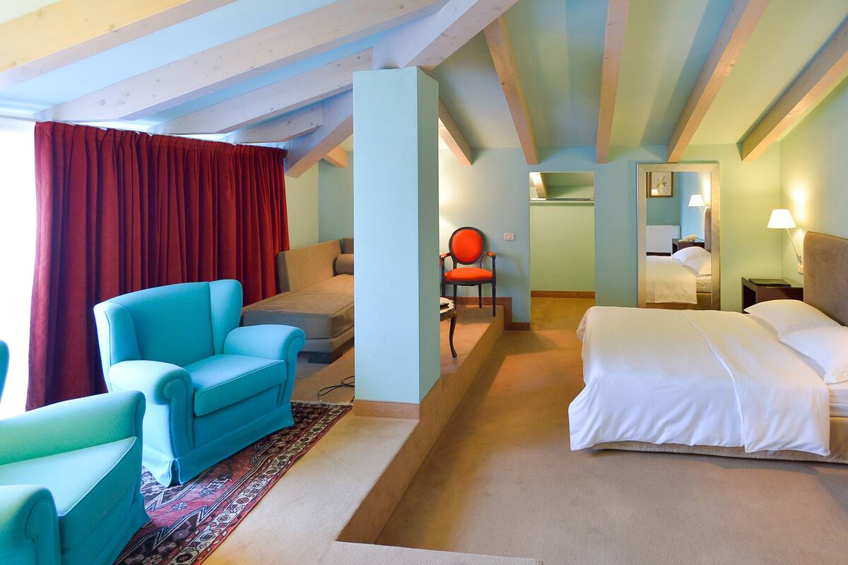 Una habitación de hotel con una cama, dos sillones, un sofá, una cortina roja y un espejo.