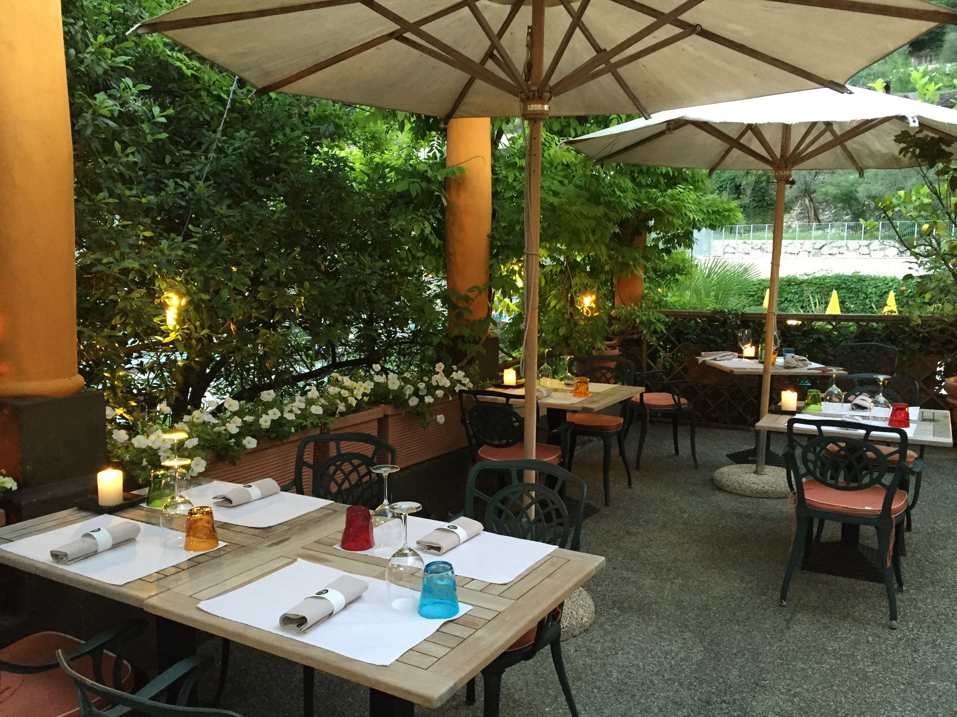 Un espace de restauration en plein air, avec des tables et des chaises, entouré de verdure et illuminé de guirlandes lumineuses décoratives.