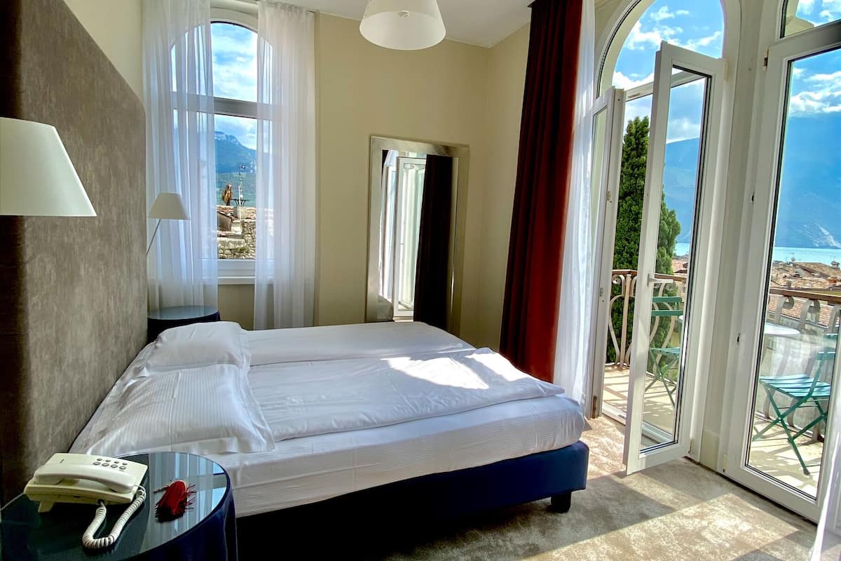 Habitación de hotel con cama, teléfono, lámpara y vistas al exterior a través de amplios ventanales.