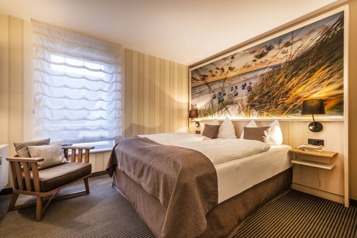 Een hotelkamer met een groot bed, een stoel, een nachtkastje, een lamp en een schilderij aan de muur.