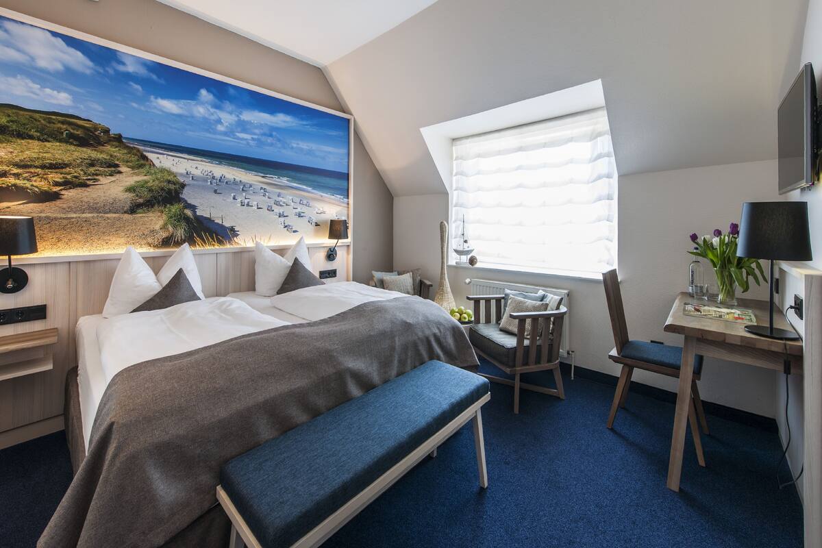 Hotelkamer met een groot bed, een bureau, een stoel, een bank, een televisie en een raam met jaloezieën.