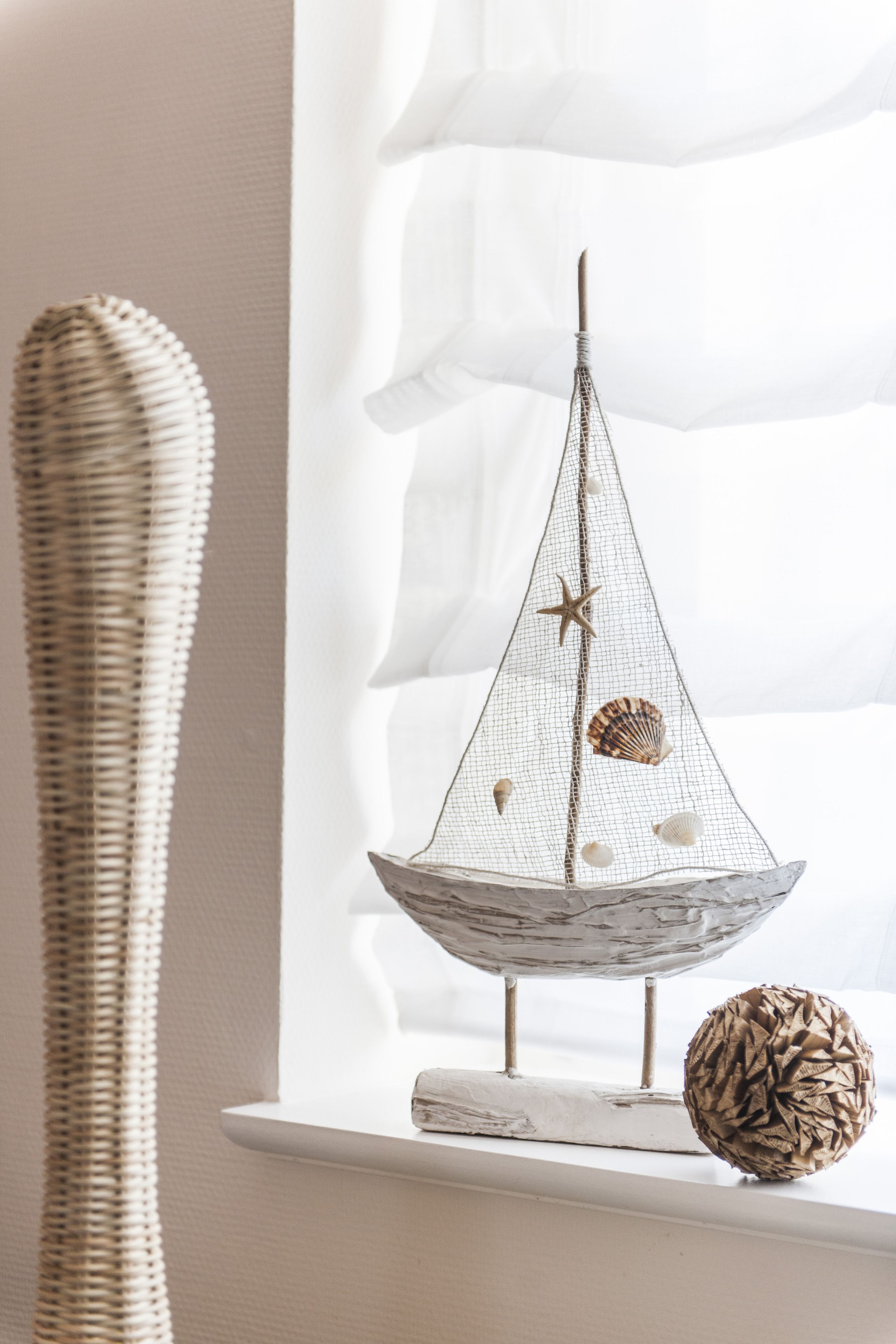 Une maquette de voilier décorative, ornée d’une étoile de mer et de coquillages, posée sur une étagère.