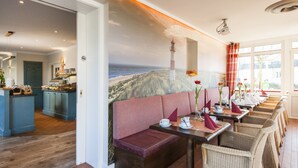 A restaurant with a coastal mural, wooden flooring, and wicker chairs.