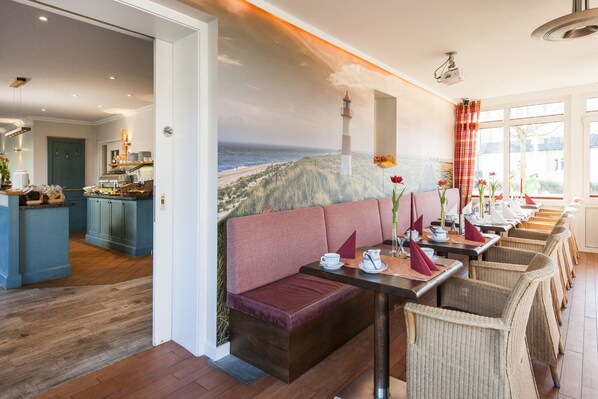 Un restaurante con un mural costero, suelo de madera y sillas de mimbre.