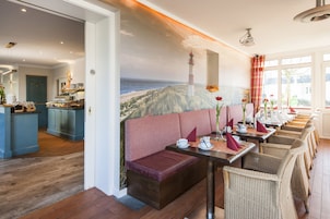 A restaurant with a coastal mural, wooden flooring, and wicker chairs.