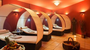 A spa room with four individual massage beds, a fruit bowl, and a candle on the floor.