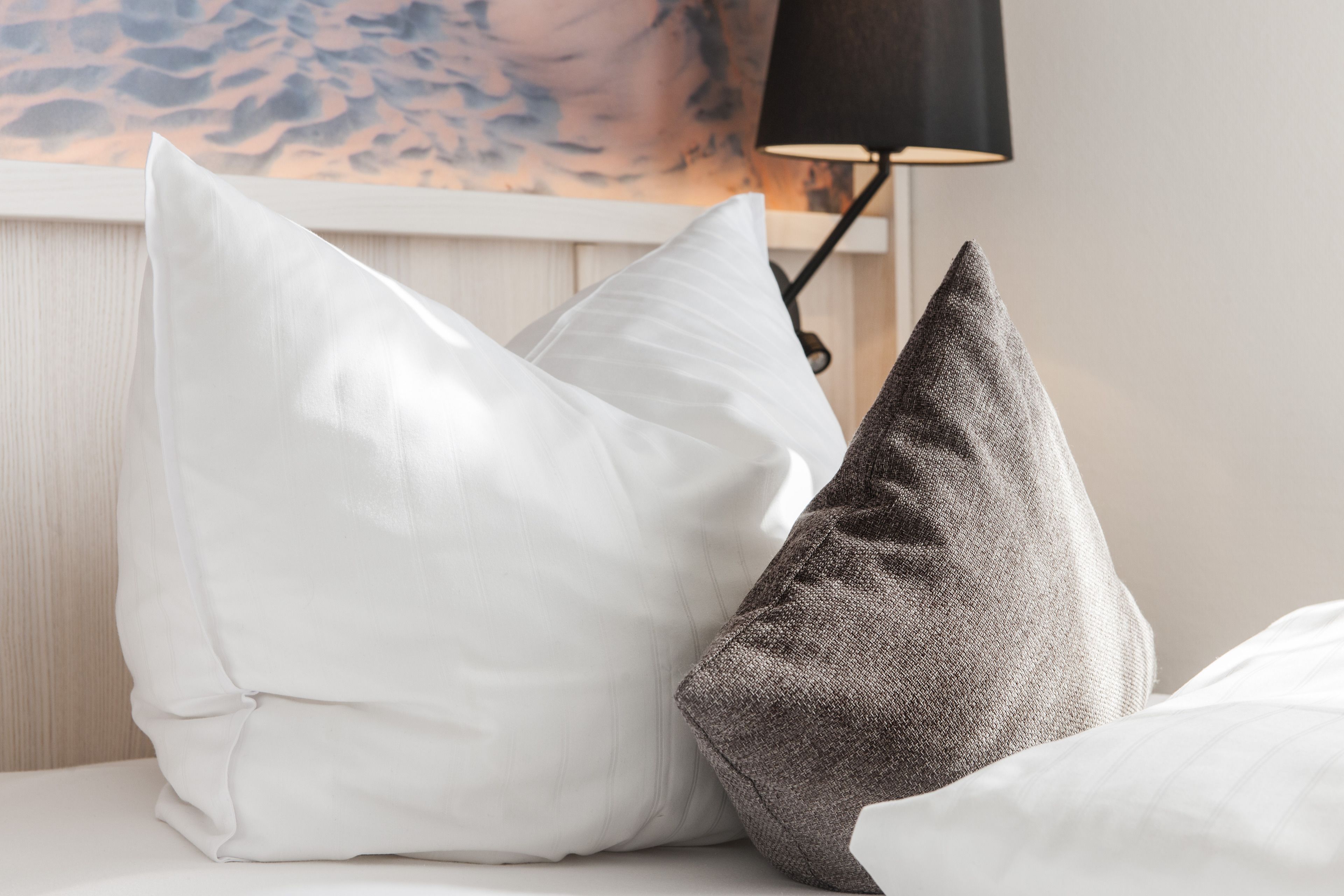 Una cama con dos almohadas, una blanca y otra gris, y una lámpara negra al fondo.