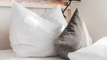 Una cama con dos almohadas, una blanca y otra gris, y una lámpara negra al fondo.