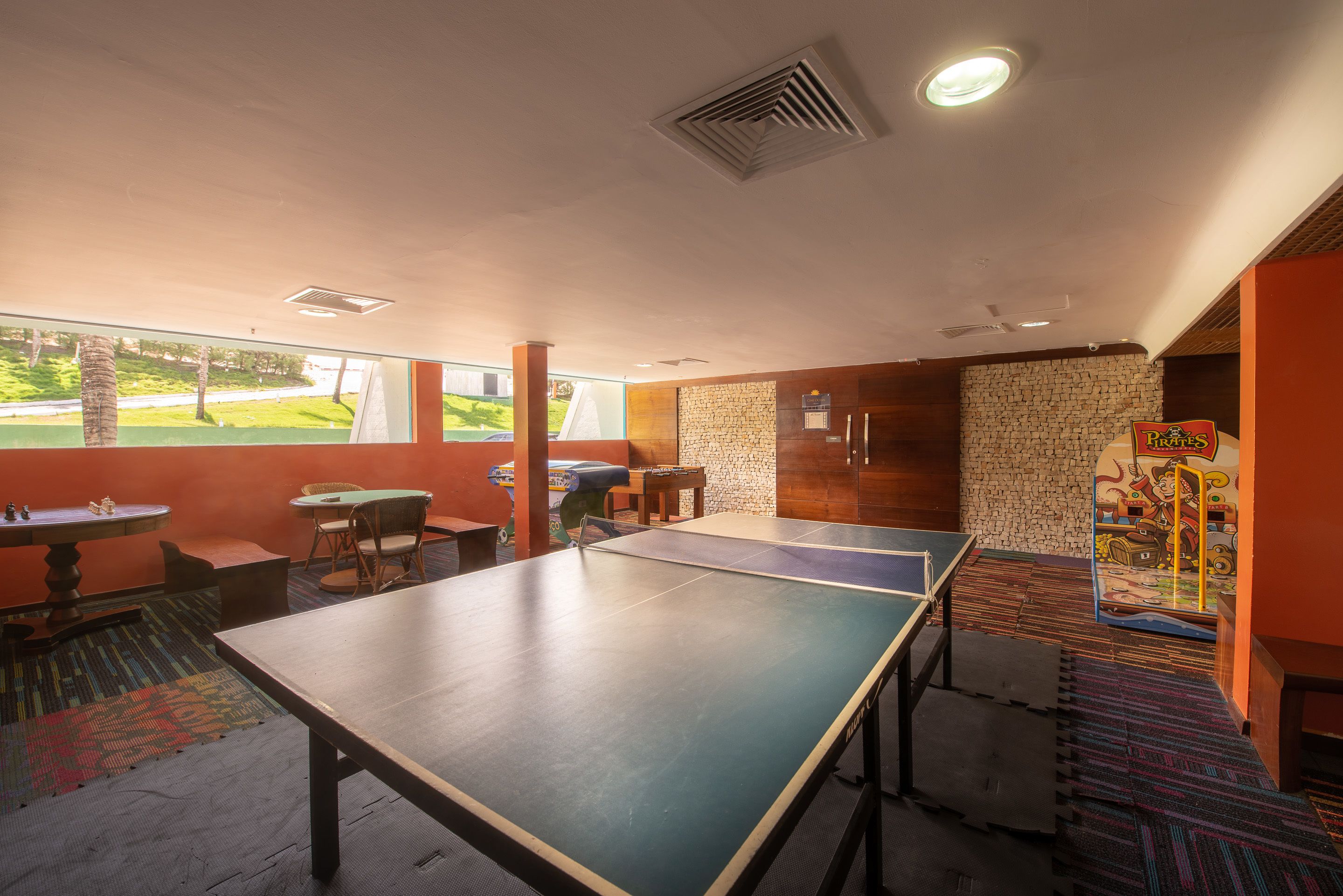 A ping pong table in a room with a view of a golf course, a brick wall, and a mural.