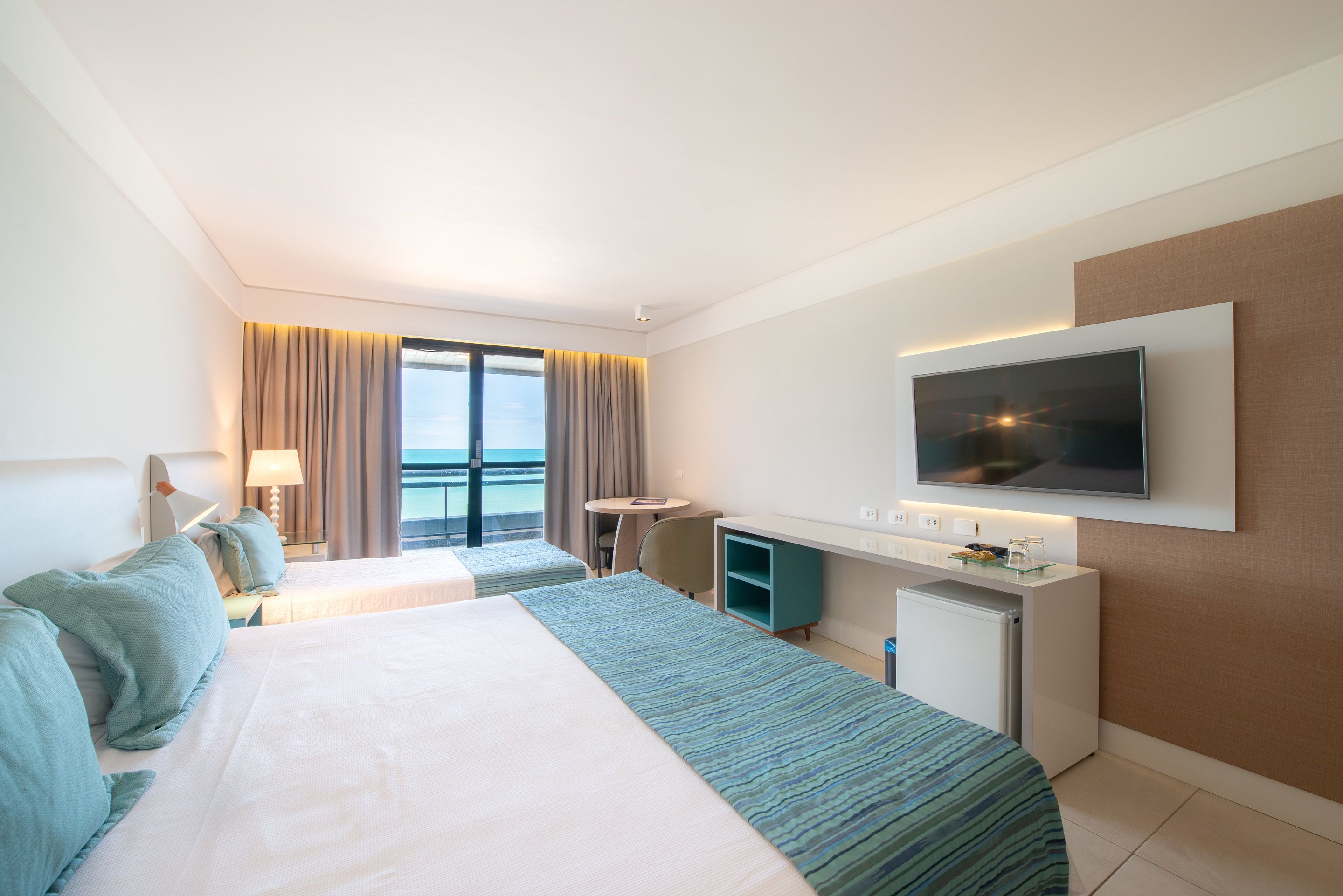 Habitación de hotel con dos camas, un escritorio, un televisor y vista al océano.