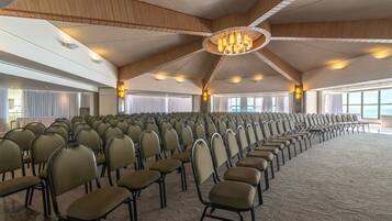 A large hall with rows of chairs, a high ceiling with wooden beams, and a central chandelier.