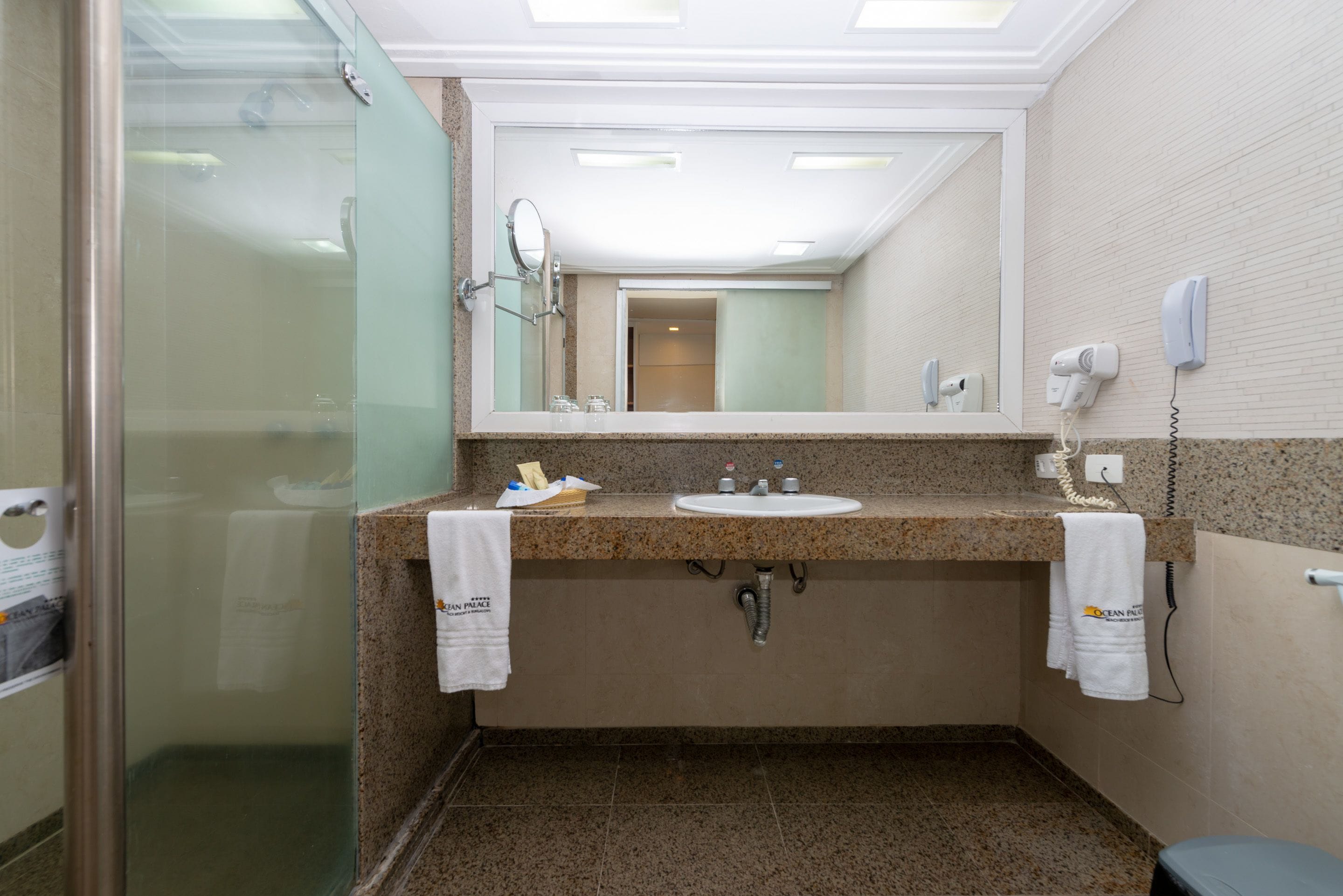 A bathroom with a granite countertop, a sink, a mirror, a towel rack, and a shower area.