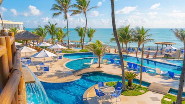 Zona de piscina de un resort con varias piscinas, palmeras y sillas de descanso.