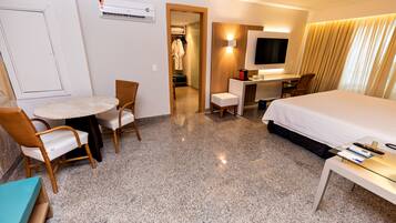 Quarto de hotel com uma cama, escrivaninha, cadeira, mesa e televisão.