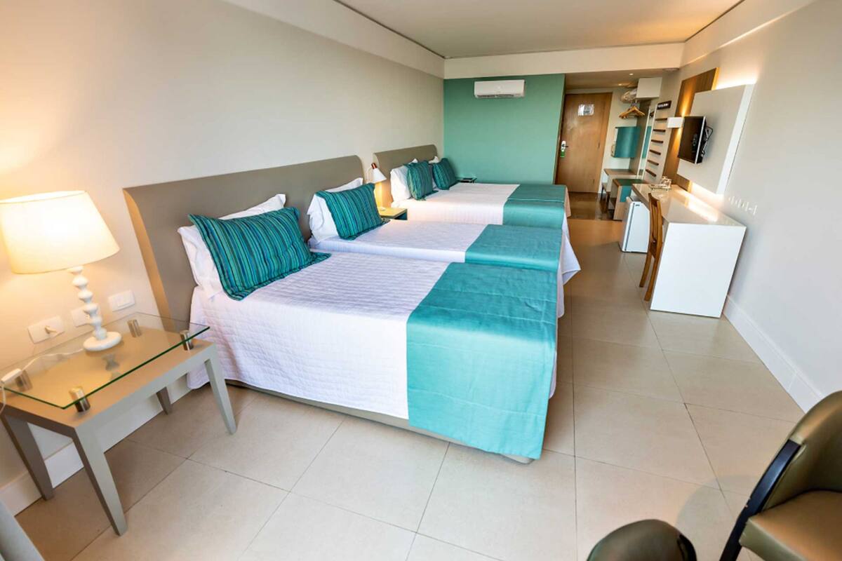A hotel room with two beds, a desk, a chair, a TV, and a kitchenette.