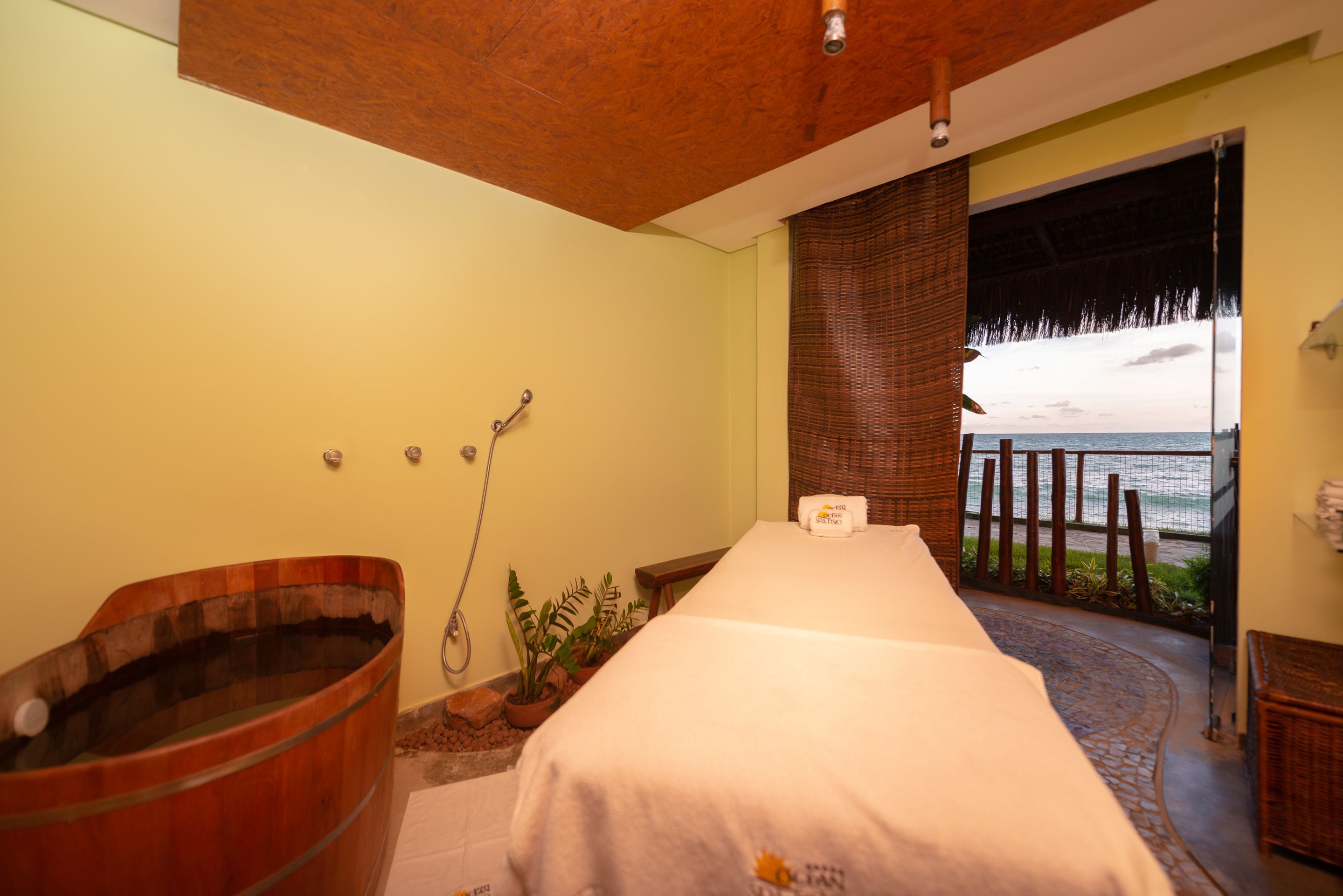 Um quarto de spa com uma banheira de madeira, uma mesa de massagem e vista para o oceano.