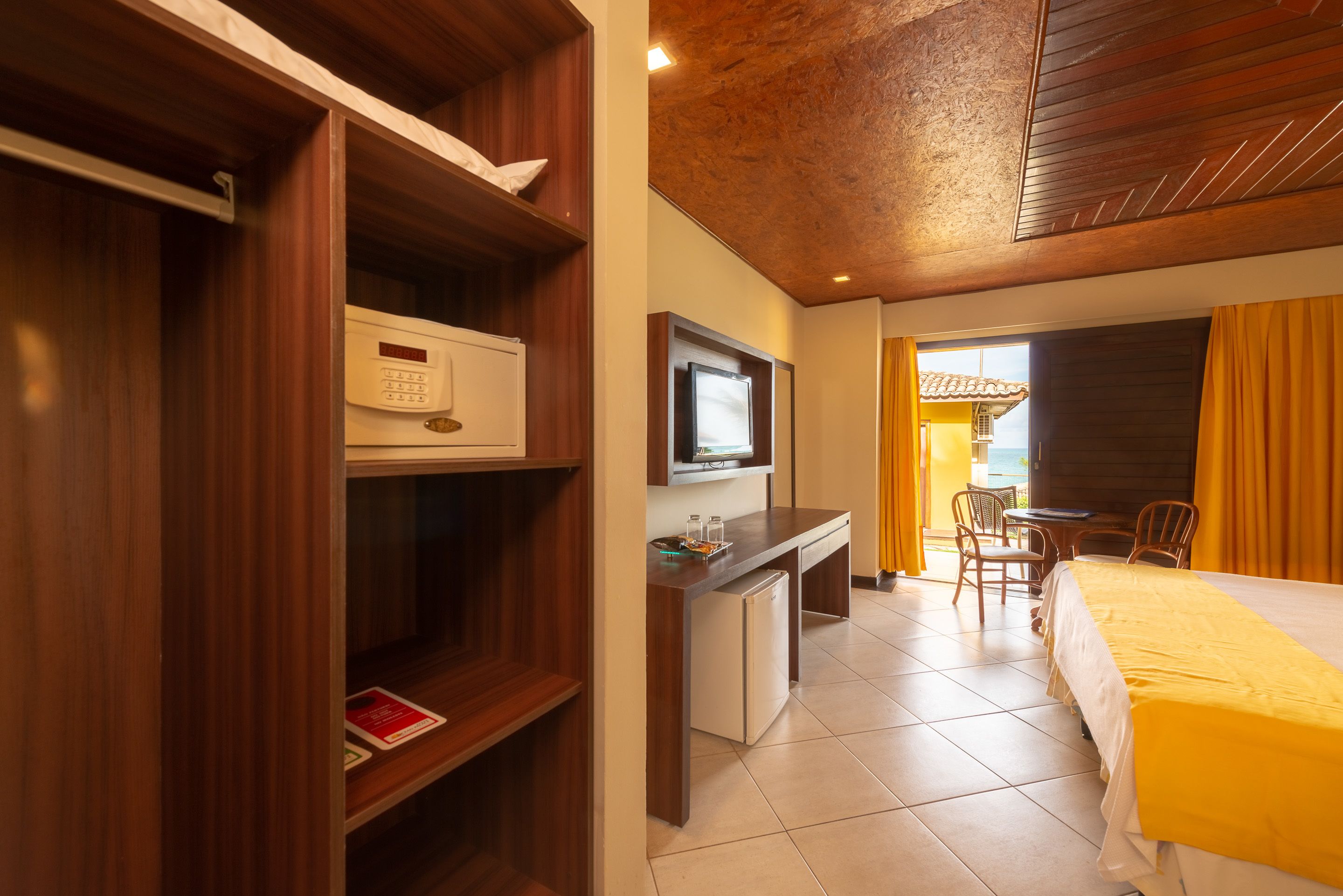 A hotel room with a wooden desk, a television, a bed with a yellow bedspread, and a view of the outdoors.