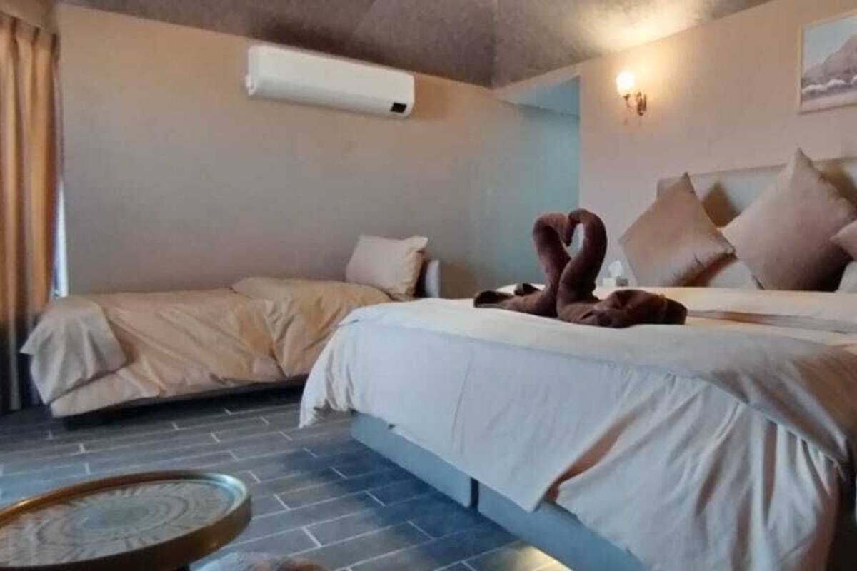 A hotel room with a bed, a smaller bed or sofa, a round table, and a wall-mounted air conditioner.