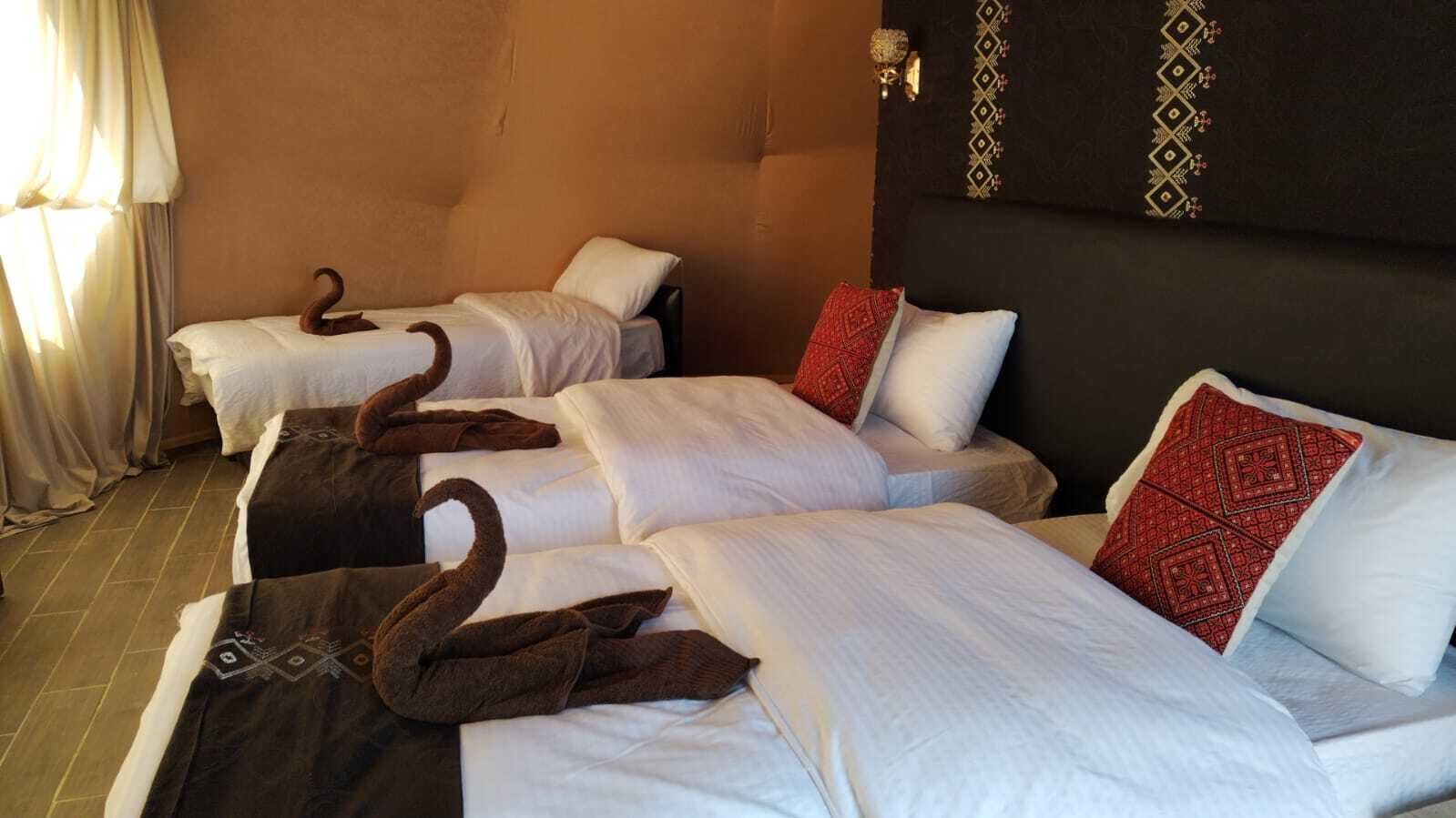Une chambre d’hôtel avec trois lits, chacun agrémenté de draps blancs et d’oreillers décoratifs, dont un oreiller à motifs rouges.
