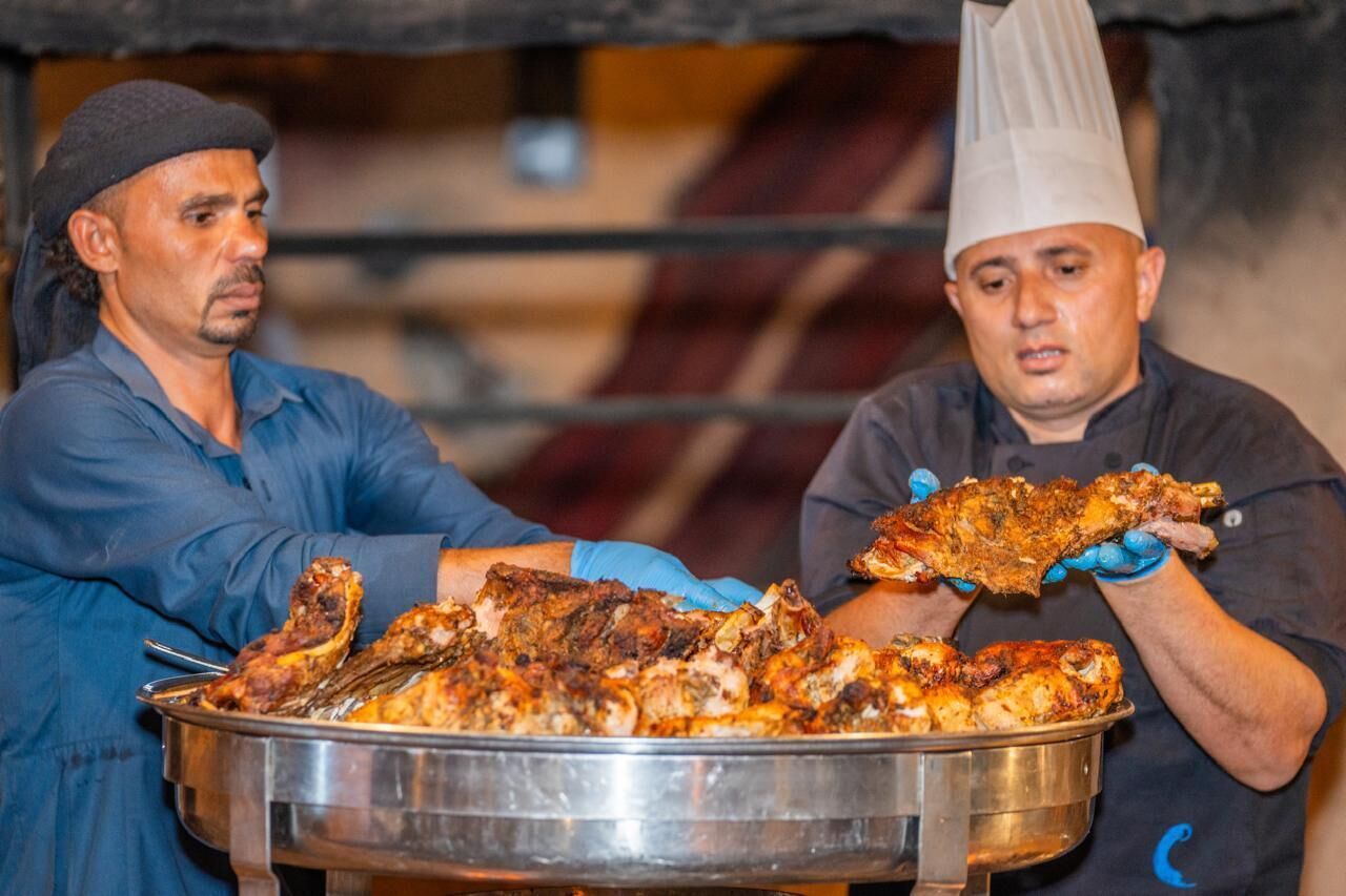 Due persone che maneggiano un grande vassoio di carne arrosto.
