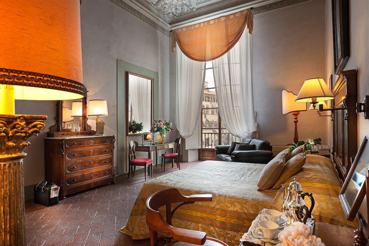 Une chambre d’hôtel avec un lit, un bureau, une chaise, une commode et une fenêtre avec des rideaux.