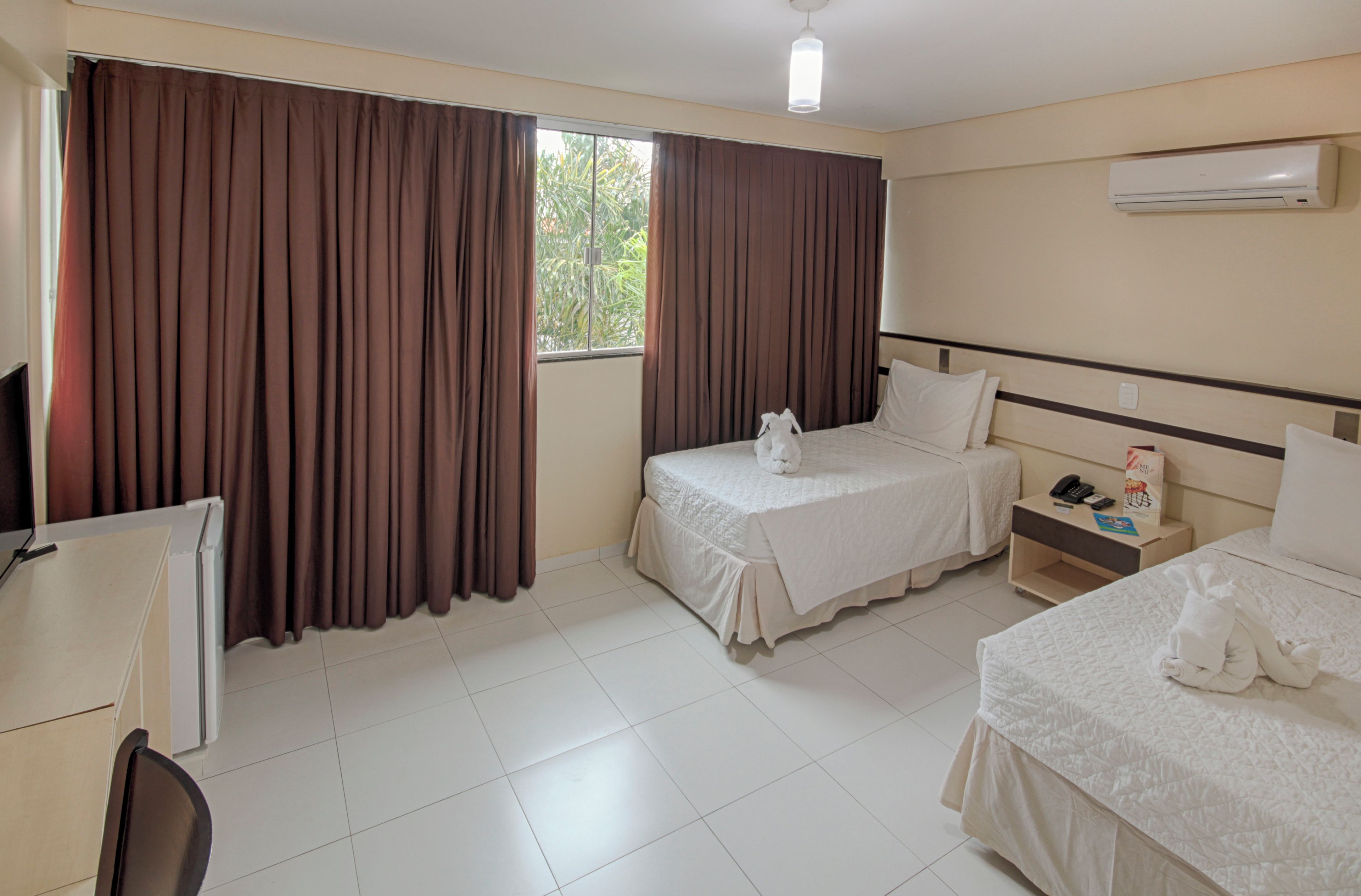A hotel room with two beds, a desk, a chair, and an air conditioning unit.