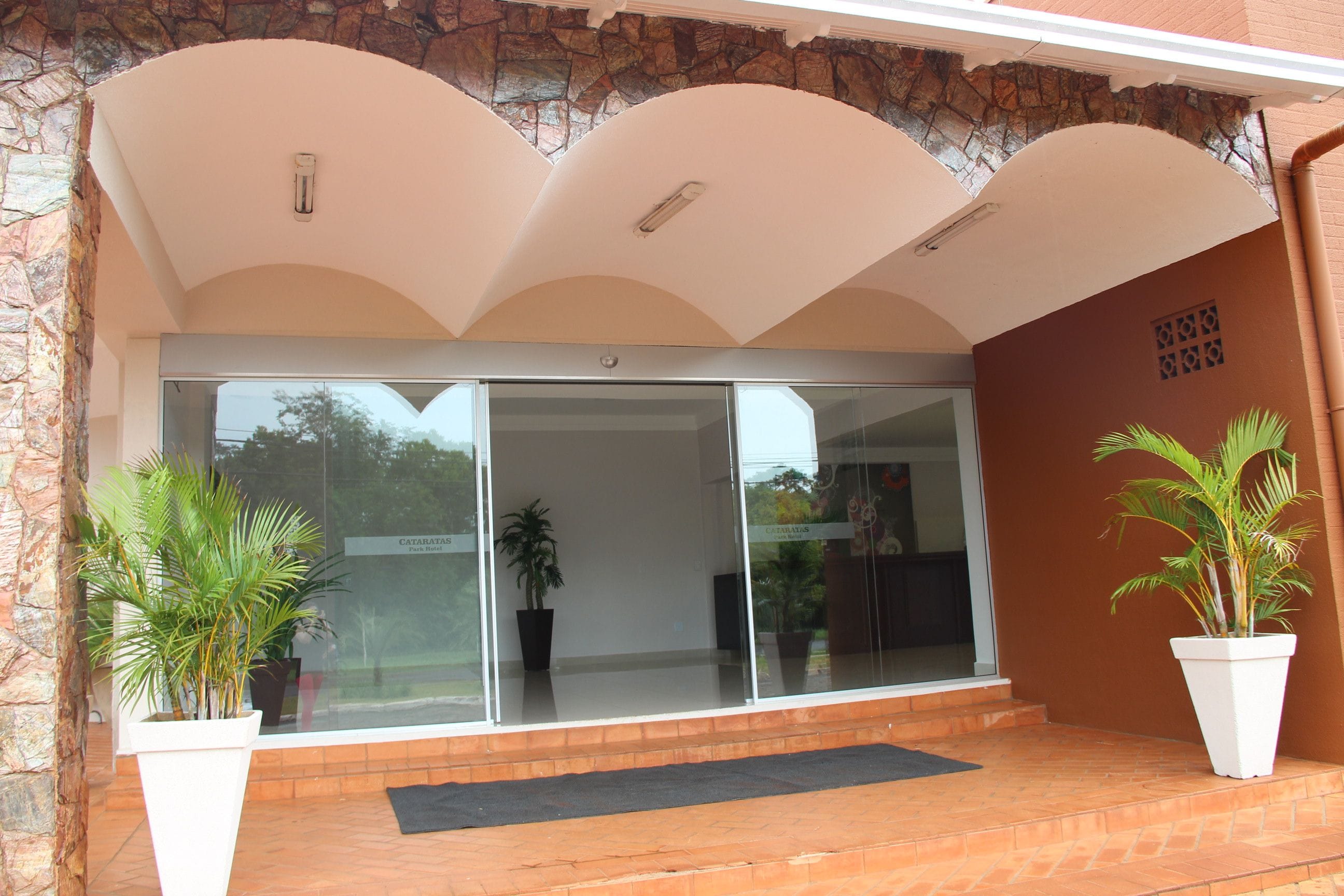 A hotel entrance with a stone facade, a glass door, and potted plants.