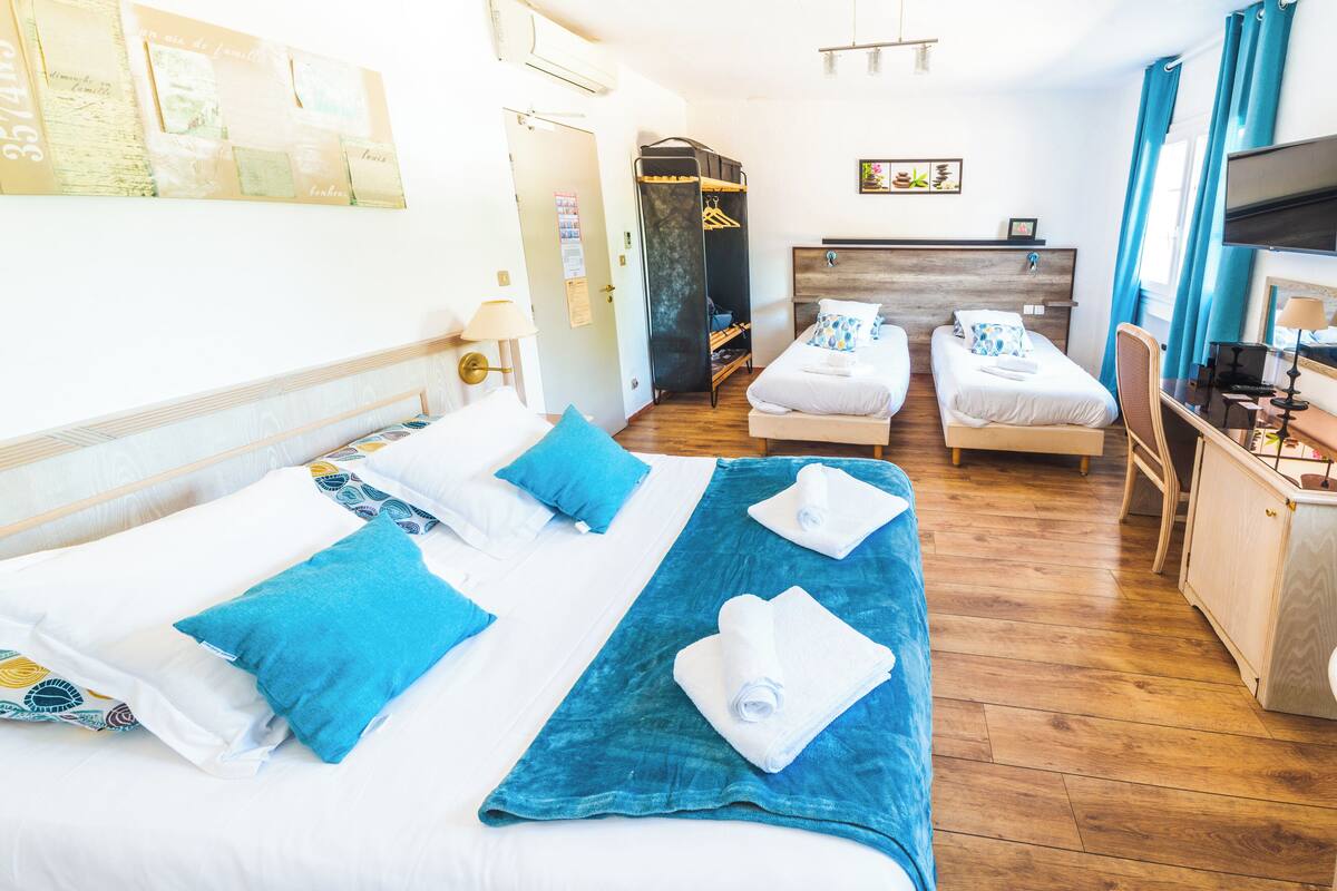Una habitación de hotel con una cama grande, dos camas individuales, un armario, un escritorio con silla y un televisor.