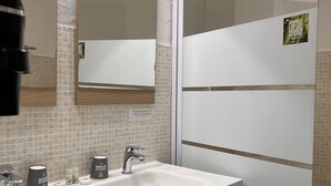 A modern bathroom with a white sink, two faucets, and a mirror above. There are wooden cabinets below the sink and a towel rack to the right. - La Bastide des Golfs (Grasse)