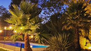 A swimming pool surrounded by palm trees and a fence at dusk. - La Bastide des Golfs (Grasse)