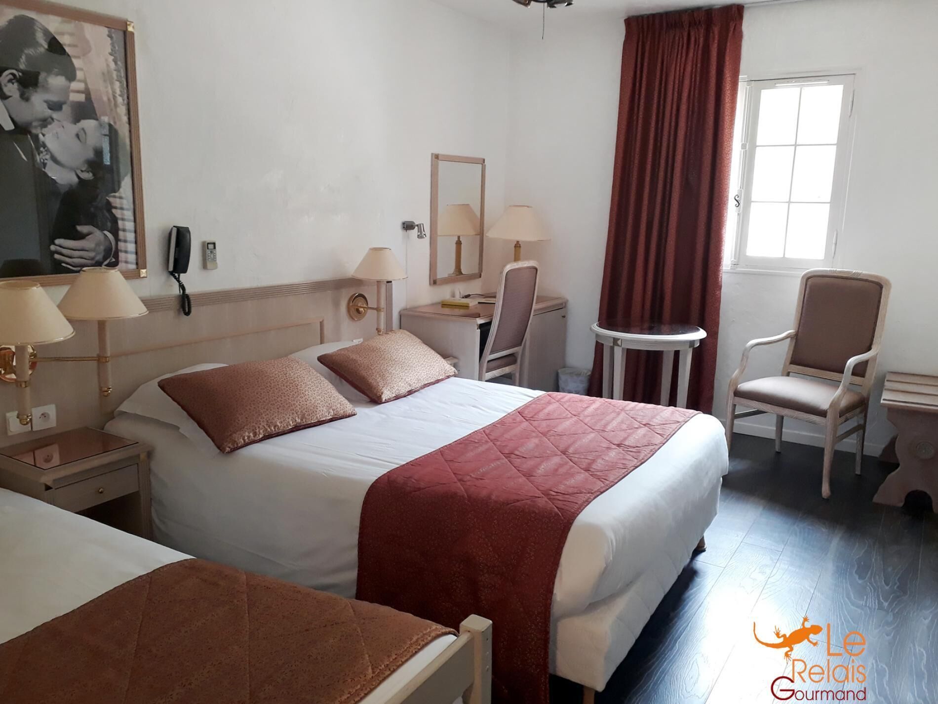 A hotel room with a bed, bedside tables, a desk, a chair, a mirror, and a window with curtains.