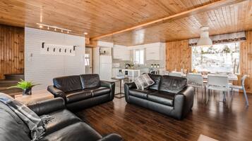 A spacious living area with leather sofas, a dining table, and a kitchen in the background.