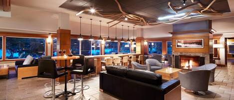 A modern lounge area with a fireplace, bar seating, and a large window overlooking a cityscape.