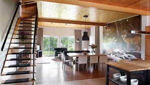 Un interior moderno con una escalera de madera, zona de comedor con vistas y un mural grande de un lobo.