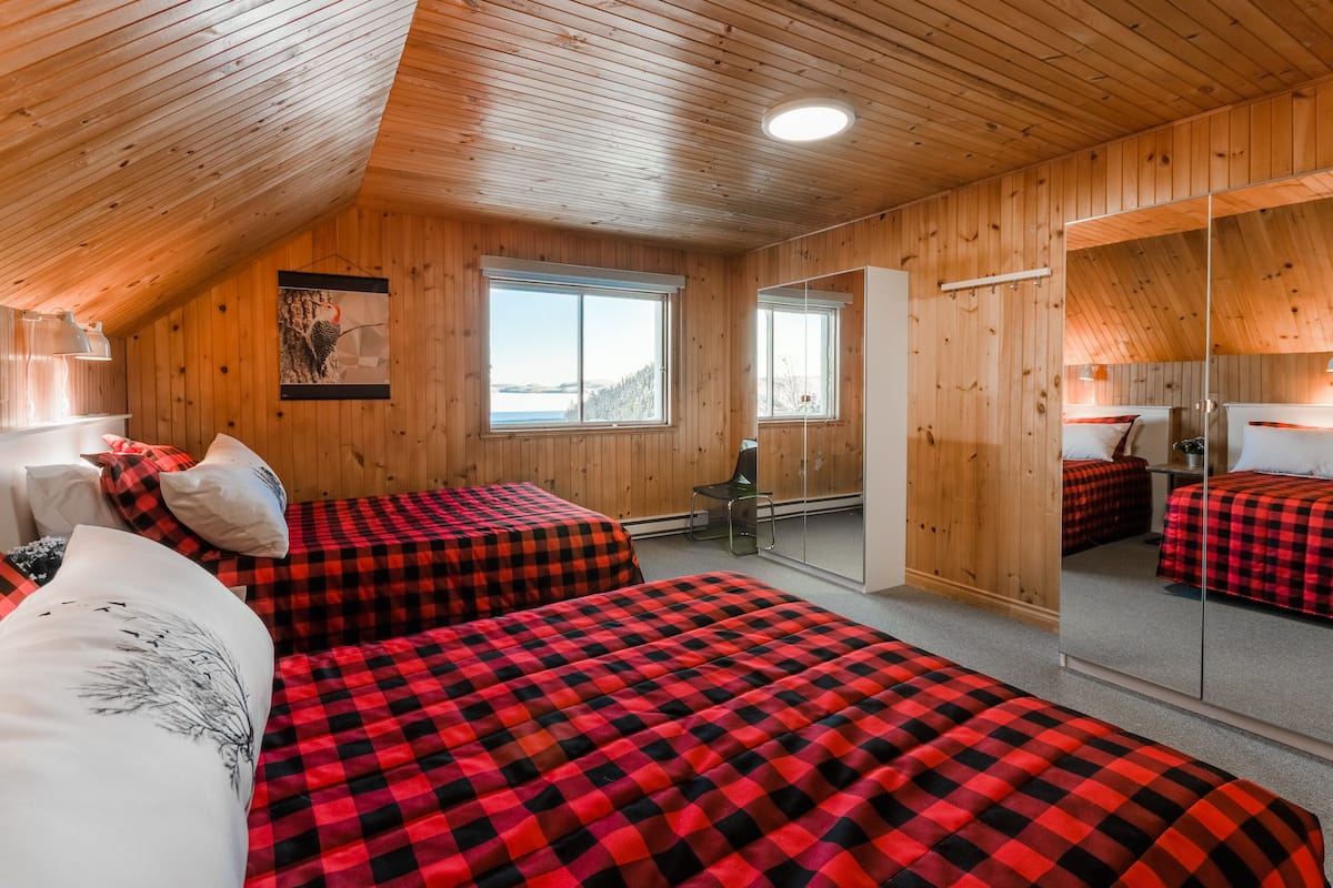 A wooden cabin with two beds, a large window, a mirror, and a view of the outdoors.