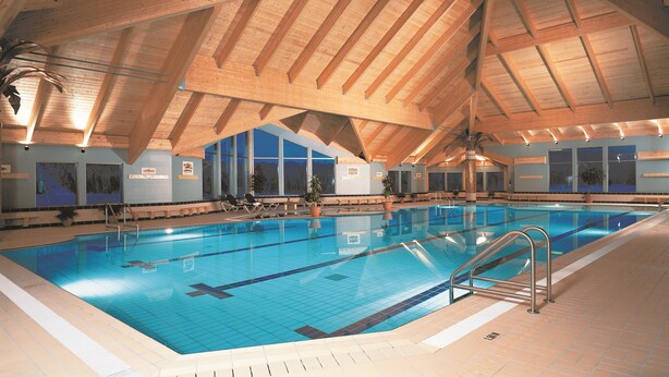 Una piscina interior con vigas de madera y ventanas amplias.
